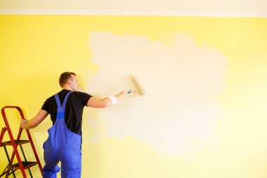 Erkek uzman duvarları kapalı alanda boyuyor, tamir konsepti var.
