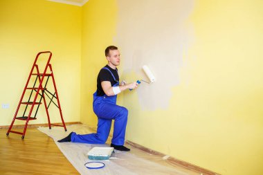Bir adam evin duvarını silindir ve boyayla boyuyor. Evdeki odaların yenilenmesi.