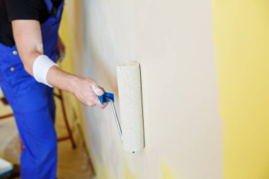 Tulumlu genç adam boya silindiri tutuyor. Apartman odası tadilatı için alet edevat. Ev yenileme konsepti