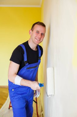 Tulumlu genç adam boya silindiri tutuyor. Apartman odası tadilatı için alet edevat. Ev yenileme konsepti