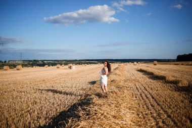 Buğday tarlasında genç kıvırcık saçlı bir kadının portresi, buğdayın biçildiği ve demetlerin dikildiği, doğanın tadını çıkardığı yer. Doğa. Güneş ışınları Tarım