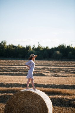 Köyde buğday tarlalarında parke ve gökyüzüyle poz veren çekici bir kadın. Hasattan sonra tarlada saman balyası