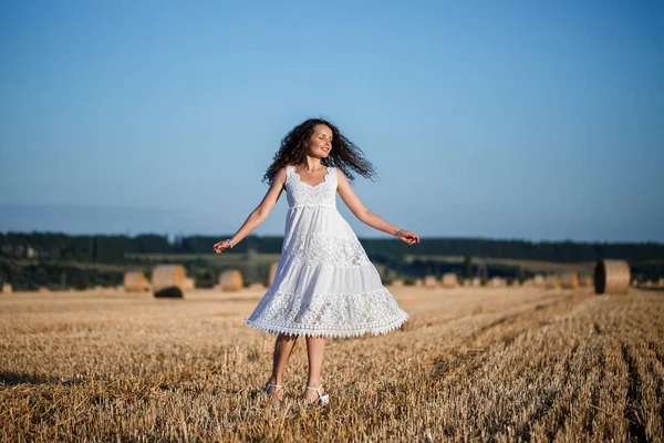 白い夏のドレスを着た若い美しい女性が 干草の巨大な色合いの白い小麦畑に立って自然を楽しんでいます 村の自然 選択的焦点 — ストック写真