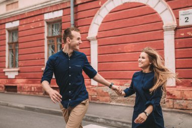 Birbirine aşık mutlu evli bir çift caddede koşar ve sevinir. Güzel genç bir çift el ele tutuşuyor ve gülümsüyor.