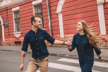 Birbirine aşık mutlu evli bir çift caddede koşar ve sevinir. Güzel genç bir çift el ele tutuşuyor ve gülümsüyor.