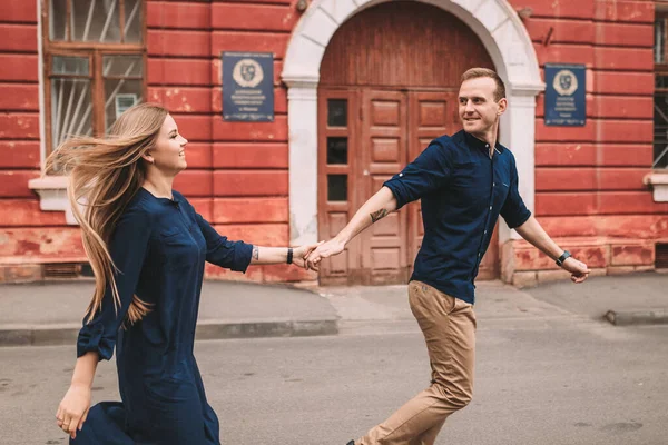 愛の幸せな夫婦が通りを走り 喜びます 街の通りを歩いていると 美しい若いカップルが手を取り合って笑っている — ストック写真
