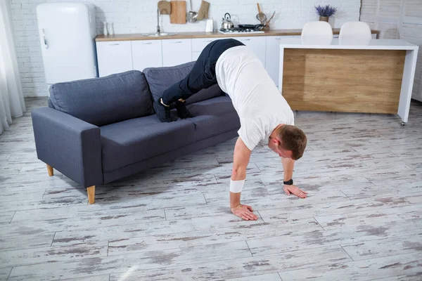 A young man goes in for sports at home, he does push-ups on the couch. Healthy lifestyle