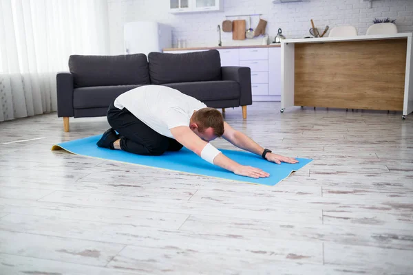 Young man sitting on carpet in his home and doing stretching after sports