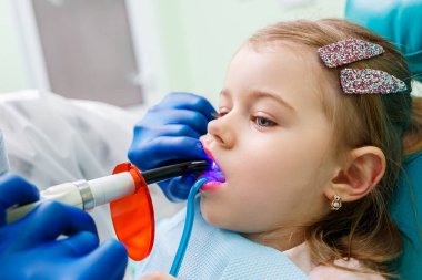 Profesyonel bir doktor, bir çocuk dişçisi, küçük bir kızın dişlerini aletlerle tedavi ediyor. Hasta muayenesi için dişçi ofisi. Bir çocukta diş tedavisi süreci