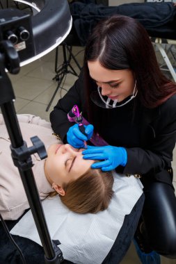 Güzellik salonunda gür kaşları olan güzel bir kadının yüzü. Kaşlar için kalıcı makyaj. Güzellik uzmanı kadınlar için kaş dövmesi yapar. Güzellik prosedürü.