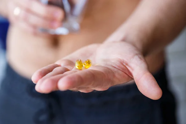 A young man holds vitamins and a glass of water in his hands. Immunity pills