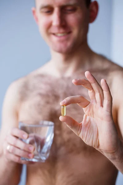 A young man holds vitamins and a glass of water in his hands. Immunity pills