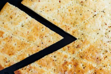 Siyah taşlı arka planda dilimlenmiş pizza, üst manzara. Peynirli taze pişmiş Focaccia.