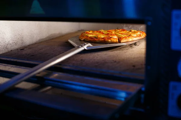 Heiße leckere amerikanische Pizza mit Tomatenkäse und Fleisch mit dicker Kruste auf einer Metallschaufel, der Bäcker holt die Pizza aus dem Ofen — Stockfoto