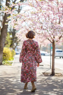 Şehrin sokaklarındaki ağaçta çiçeklerle sakura dalları. Çiçekli sakurayla sokakta dönen mutlu bir kadın. Sakura çiçekleri.