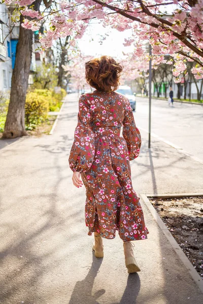 桜は街中の木の上に花を咲かせます 桜が咲く通りを回転する幸せな女性の女の子 — ストック写真