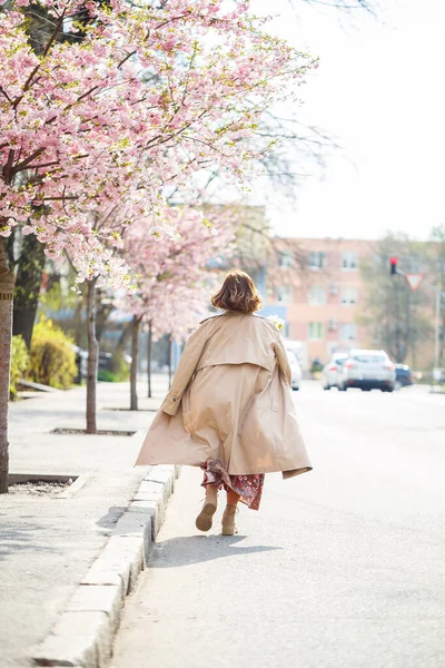 春になると 桜の咲く通りを女が歩いている 長い絹のエレガントなヴィンテージのドレスの女の子が開花木の間を歩く — ストック写真