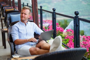 Duygusal bir adam tatilde bilgisayarın başına oturur ve çalışır. Freelancer tatildeyken çalışıyor