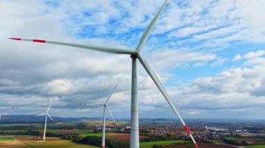 Büyük rüzgar türbinleri rüzgar enerjisini zapt ederken aşağıdaki yemyeşil alanlar da temiz enerji üretimini destekleyen sakin ortama derinlik katar.