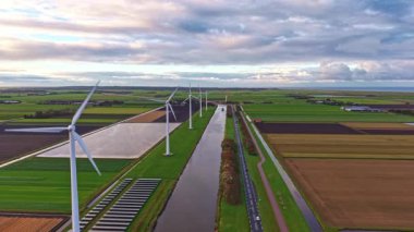 Bereketli bir arazide nefes kesici rüzgar türbinleri manzarası Geniş alanlar, dolambaçlı bir kanal ve doğanın ve teknolojinin dengesini vurgulayan bulutlu bir gökyüzü.