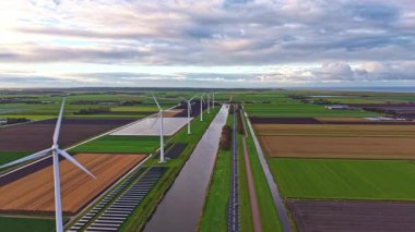 Parlak yeşil tarlalar, rüzgar türbinleriyle benekli meltemde yavaşça sallanan sakin bir kanal, dolambaçlı bir yola paralel döner ve sakin bir kırsal alan yaratır.