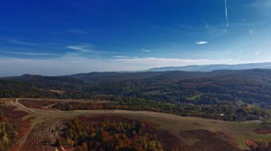 Parlak mavi gökyüzünün altında, parlak sonbahar yapraklarıyla kaplı yuvarlanan tepeler bu sakin kırsal alanda güzelliğini sergiliyor.