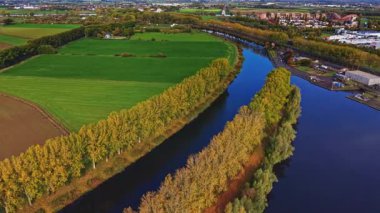 Güzel bir nehir yılanları canlı yeşil tarlalarda ve sıra sıra altın ağaçlarda berrak gökyüzü doğayı ve şehir yaşamını uyum içinde gösteren uzak bir şehir alanını gözler önüne seriyor.