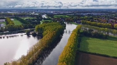 Büyüleyici bir manzara, altın ağaçların ve canlı tarlaların arasında dolanan bir nehri yakındaki küçük köprüler birbirine bağlıyken gökyüzünün güzelliğini yansıtır.