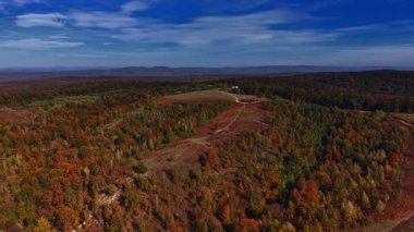 Sonbahar renkleriyle süslenmiş geniş bir kırsal manzara Rolling Hills, uzak bir çiftlik evine doğru giden kirli bir patika ile kırmızı turuncu ve sarı ağaçların bir karışımını gösteriyor.