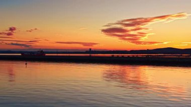 Güneş batarken sakin bir manzara beliriyor. Gökyüzünde ve suda parlak renkler bırakıyor. Bir gemi, sakin koyda dalgalanmalar yaratarak sorunsuzca süzülüyor.