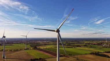 Dönen rüzgar türbinleri uçsuz bucaksız yeşil bir alanda ayakta dururlar. Koşumlu enerji kullanırlar. Yumuşak bulutlar parlak mavi gökyüzünde sürüklenirken doğanın ve teknolojinin ahenk içinde güzelliğini gösterirler.