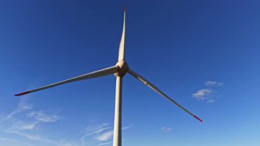 Devasa bir rüzgar türbini rüzgar enerjisinden yavaşça faydalanıyor. Bıçakları zarif bir şekilde gökyüzüne doğru uzanıyor. Sakin bulutlu sakin bir yerde yenilenebilir enerji sergiliyor.