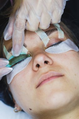 Becerikli bir güzellik uzmanı müşterinin gözlerine dikkatlice kirpik sürerek konfor sağlamak için yumuşak malzemeler kullanır. Sıcak öğleden sonra güneşi parlıyor, rahatlatıcı bir atmosfer yaratıyor..