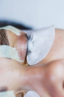 Bir müşteri kirpik uzatmaları alırken sakin bir güzellik stüdyosunda uzanıyor. Uygulama sırasında beyaz göz altı bantları cildini korumaya yardımcı olur ve barışçıl bir atmosfer yaratır..