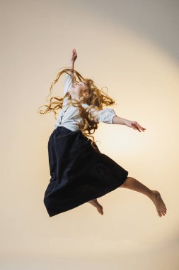 Uçan kızıl saçlı genç bir kız neşeyle havada zıplar, etek ve bluz giyer. Onun ifadesi mutluluk ve kaygısız bir ruh yayıyor..