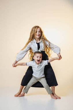 İki kardeş neşeli bir şekilde poz vererek parlak bir stüdyoda eğleniyorlar. Kız, kardeşinin elini tutarken kendine güvenerek duruyor ve yakın bağlarını gösteriyor..