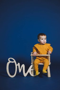 Neşeli bir çocuk, parlak sarı bir elbiseyle küçük bir sandalyede oturuyor, üzerinde 