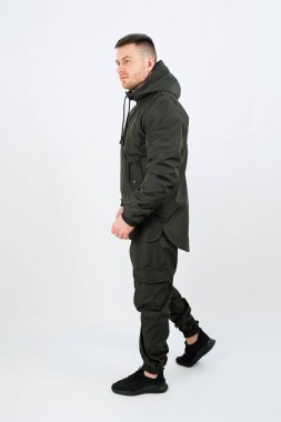 Gösterişli siyah bir ceket ve uyumlu bir pantolon giyen bir adam profilde duruyor. Minimalist bir stüdyo arka planında çağdaş şehir modasını sergilerken kendine güveni tam..