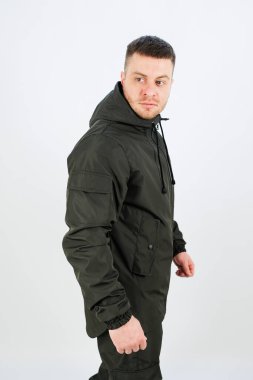 Bir adam kendine güvenen koyu renk bir ceketin içinde duruyor, kameradan uzağa bakarken güçlü bir poz sergiliyor, stüdyoda çekici ve şık bir atmosfer yaratıyor..