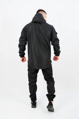 Modern siyah giyimi modelleyen bir adam stil ve pratiği birleştirir. Kıyafette kapüşonlu bir ceket ve pantalon var. Çeşitli açık hava aktiviteleri için mükemmel..