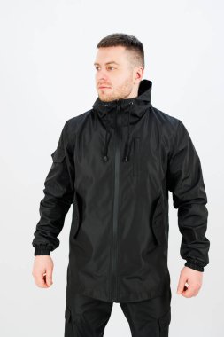 Siyah yağmurluk giyen bir adam, parlak tasarımını sergiliyor. Siyahlar, şehir ortamında güneşli bir günde moda tarzını ön plana çıkarıyor..