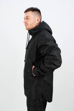 Şık bir siyah ceket giyen kendine güvenen bir adam eli cebinde durur. Onun ciddi ifadesi, genel havayı geliştiren temiz ve çağdaş arka planı tamamlıyor..