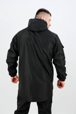 Kameraya arkası dönük bir adam modern şehir modasını ön plana çıkaran parlak siyah bir ceket giyiyor. Minimalist zemin, ceketin tasarımını geliştirir..