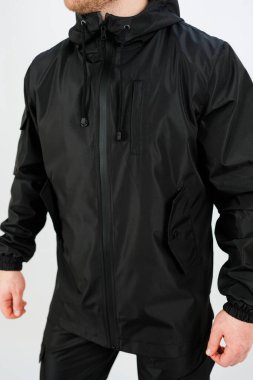 Kendine güvenen bir model parlak, siyah, su geçirmez bir ceketin içinde duruyor. Tarzı ve rahatlığı var. Temiz stüdyo arkaplanı, kentsel maceralar için mükemmel olan giysinin modern tasarımını ön plana çıkarıyor..