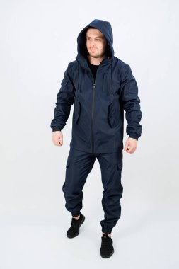 Kendine güveni olan bir adam basit bir stüdyoda duruyor, açık deniz kıyafetleri içinde stil ve pratikliği harmanlıyor. Onun duruşu kıyafetin özelliklerini ve çeşitli faaliyetler için çok yönlülüğünü vurguluyor.