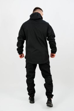 Bir insan kendinden emin bir şekilde dikilip, tamamen siyah bir sokak kıyafeti giyer. Gösterişli tasarım, düzensiz bir arkaplanda çağdaş moda eğilimlerini vurguluyor.