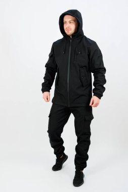 Bir adam kendine güvenen, şık siyah bir giysi ve kapüşonlu parlak, basit bir stüdyoda dikkatleri üzerine çekiyor. Kıyafet kullanım ve modayı kusursuz bir şekilde harmanlıyor..