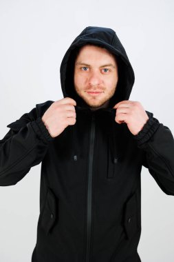 Kendine güvenen bir adam parlak siyah ceketinin kaputunu ayarlar. Ayar, parlak beyaz duvarlarla çok basit. Dikkatini tarzına ve tavırlarına veriyor..