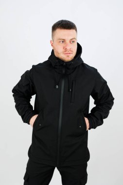Siyah ceketli, elleri cebinde modern sokak tarzını sergileyen bir adam. Temiz arka plan, kendine güvenen ifadesine ve kıyafetine odaklanmasını sağlar..