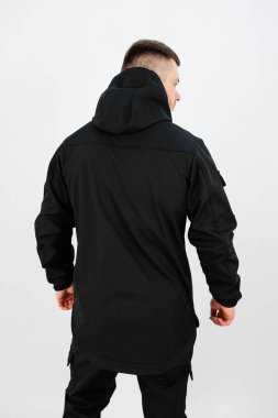 Çağdaş tasarımı vurgulayan parlak siyah bir ceket giyen bir adam basit bir stüdyoda duruyor. Ayar parlak, ceketin dokusunu ve detaylarını vurguluyor..